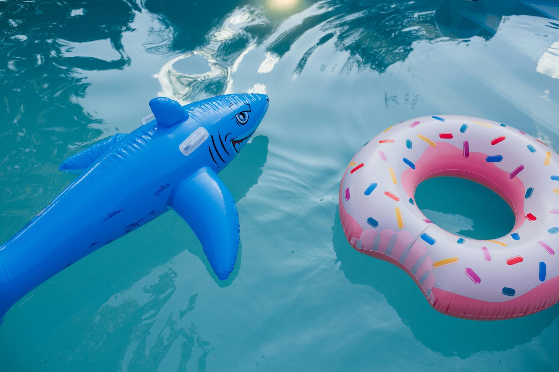 A blue shark and a pink donut float in a swimming pool.