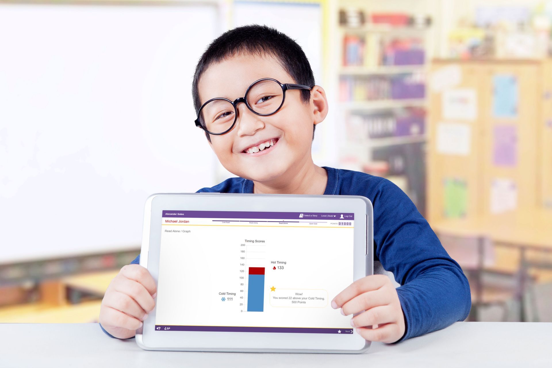 A young boy is holding a tablet computer in a classroom.
