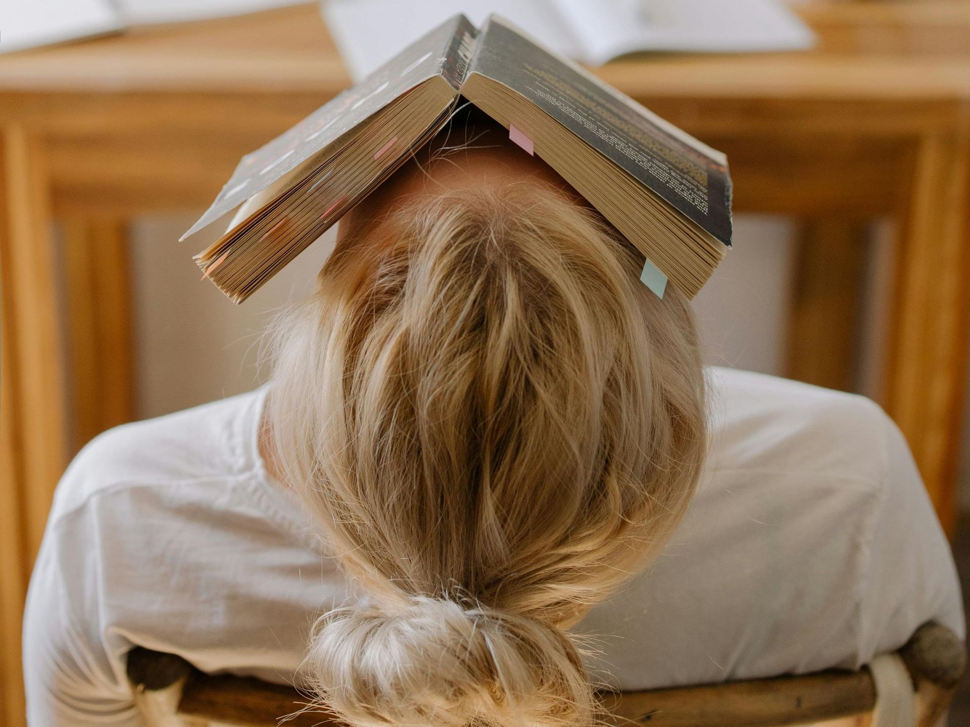 A child is sitting in a chair with a stack of books on her head.