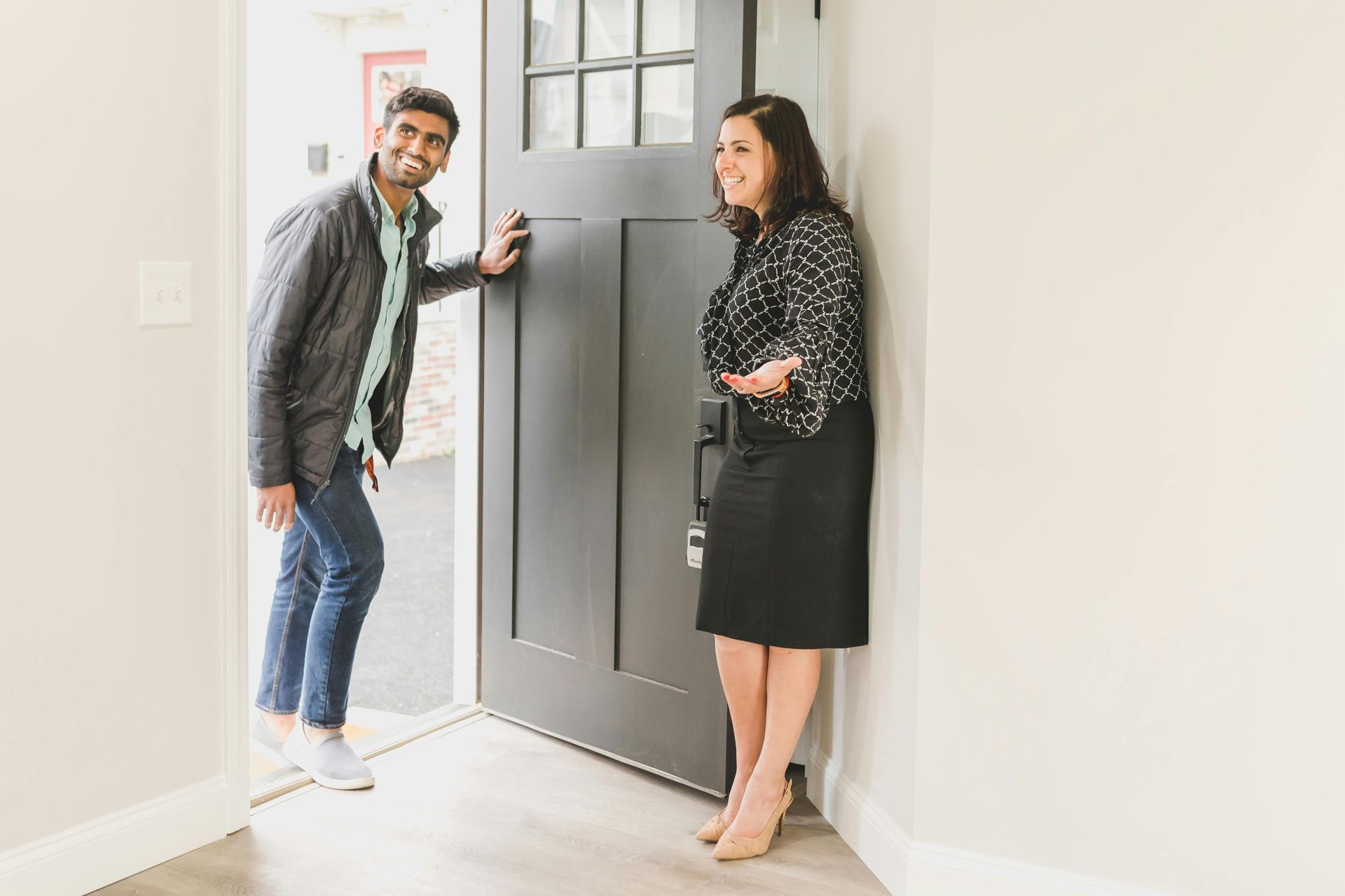 Man in doorway, woman leaning against wall, smiling. Modern home setting with black door.