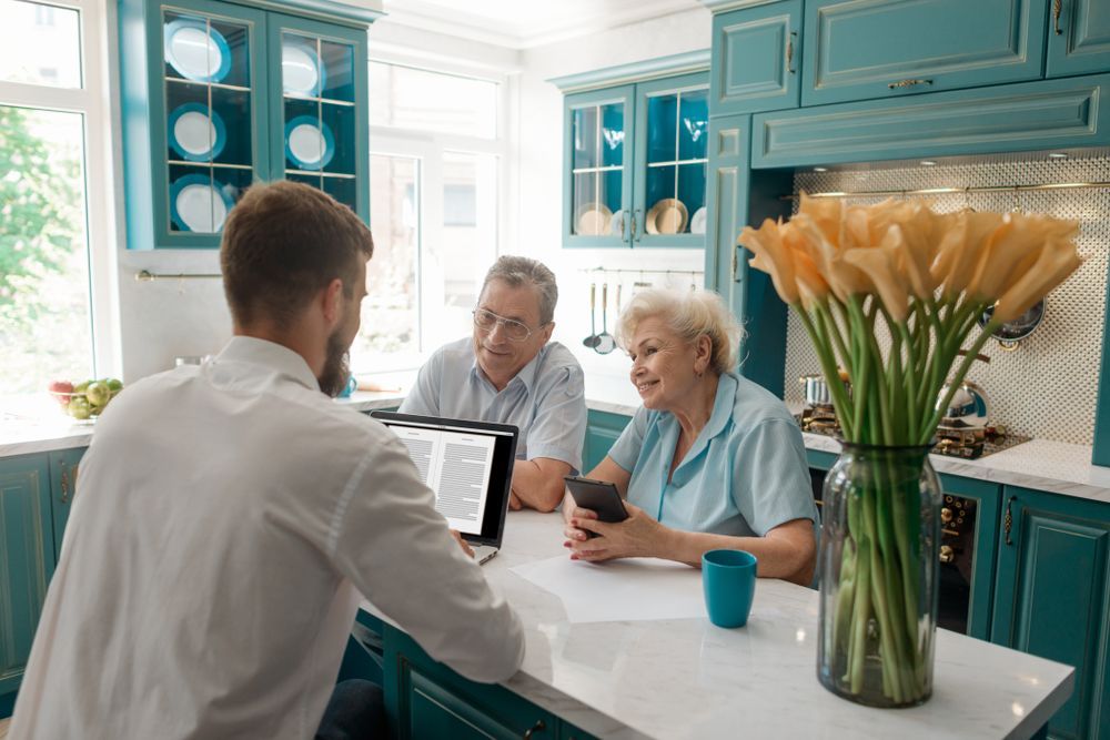 A Person Shows a Laptop to An Older Couple in A Kitchen — Freedom Wealth Solutions in Mornington, VIC
