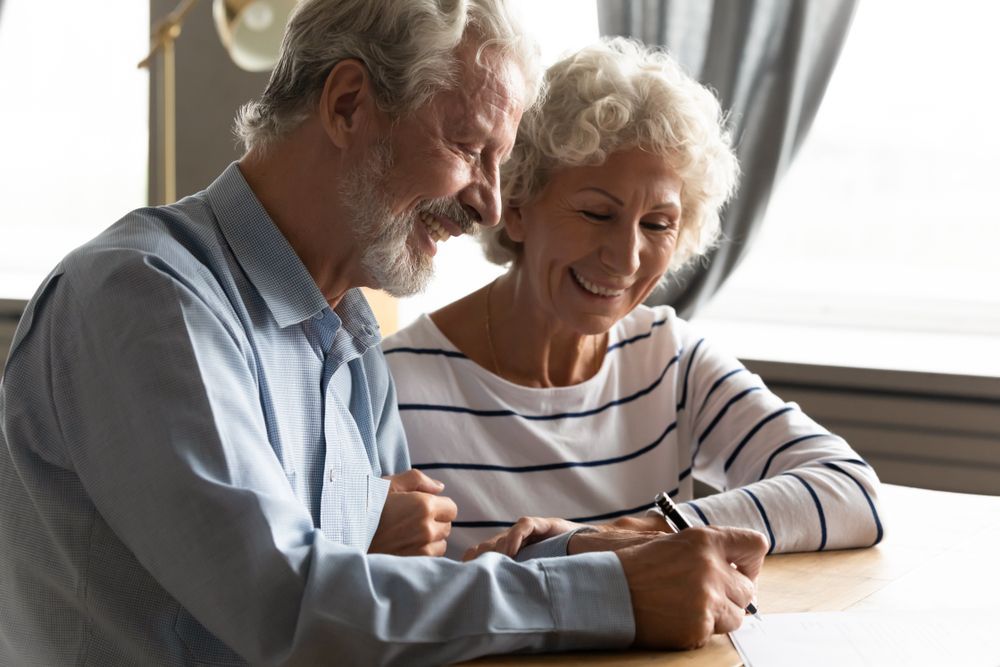 Smiling Older Couple Reviewing Paperwork Together at A Table — Freedom Wealth Solutions in Mornington, VIC