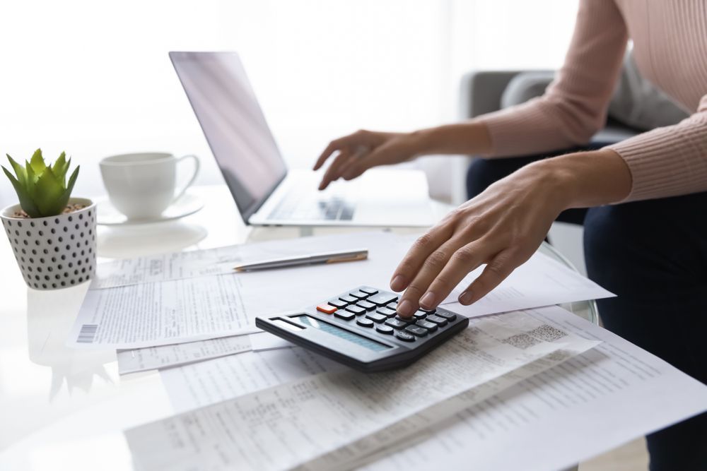 Woman Using Calculator and Laptop at A Desk with Papers — Freedom Wealth Solutions in Mornington Peninsula, VIC