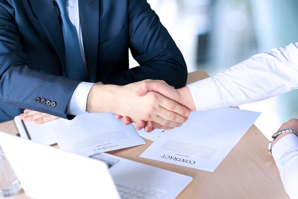 Two People in Suits Shaking Hands Over a Table with Documents — Freedom Wealth Solutions in Leongatha, VIC