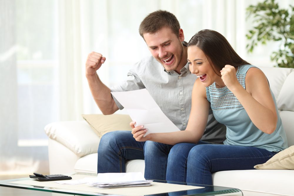 Couple on Sofa Celebrates, Looking at Paperwork with Raised Fists — Freedom Wealth Solutions in Mornington, VIC