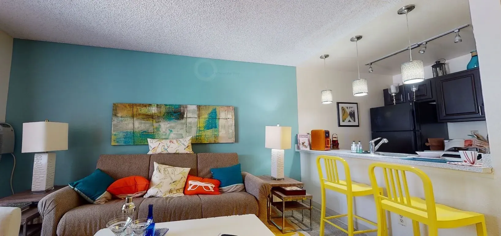 Modern living room with teal accent wall and kitchen bar with yellow stools.