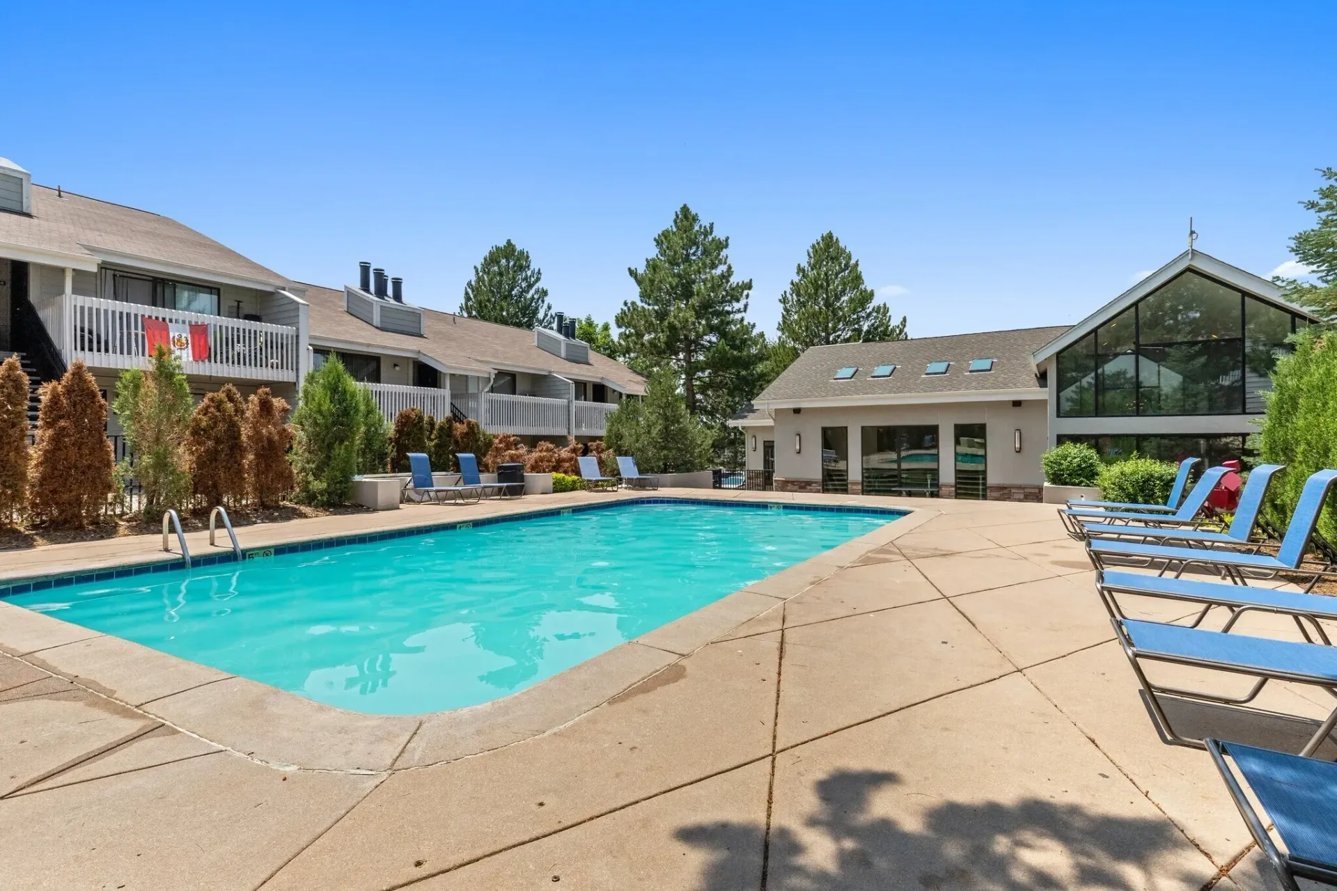 Outdoor swimming pool with lounge chairs and apartment buildings in the background.