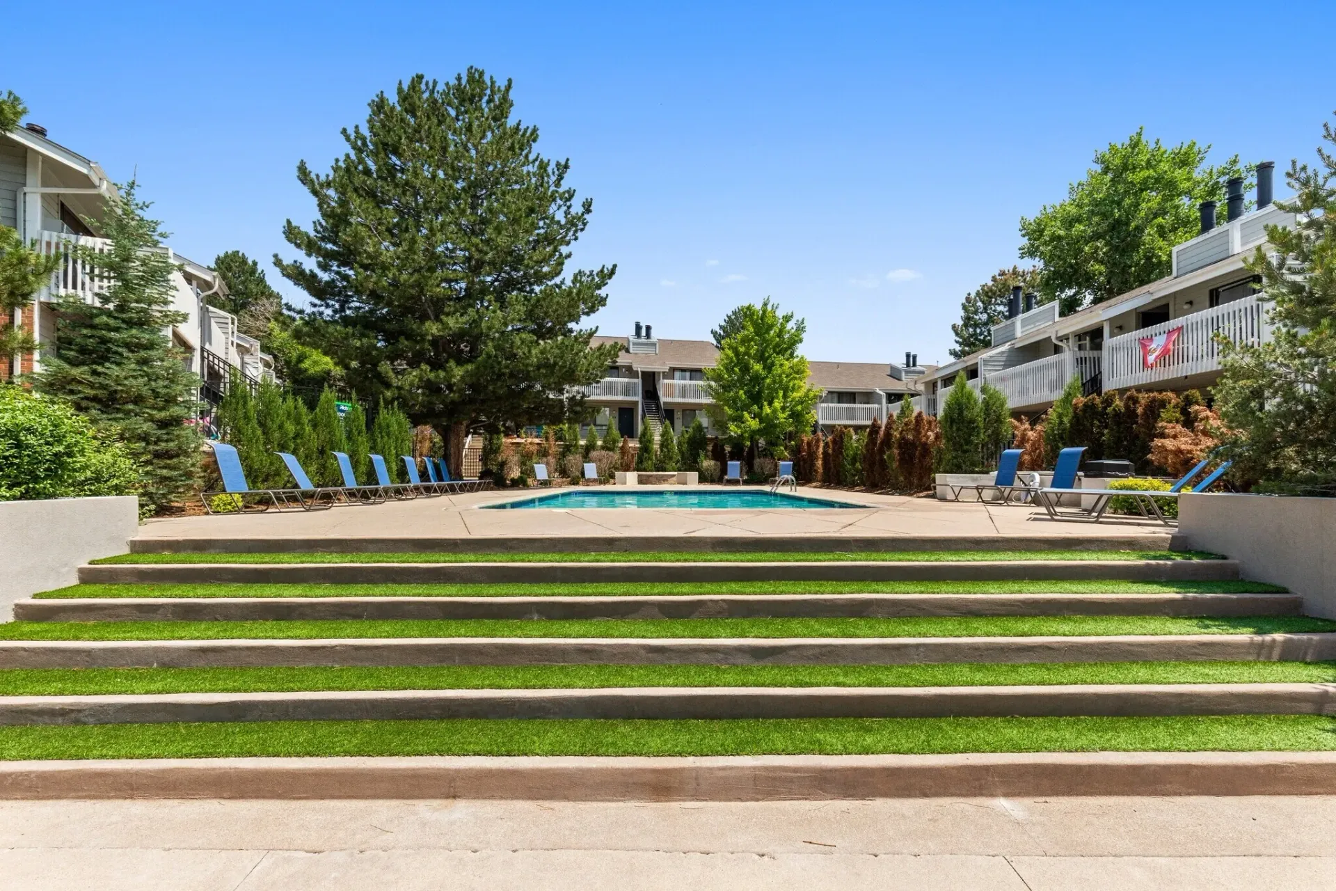 Outdoor swimming pool area with lounge chairs and tiered grass steps.