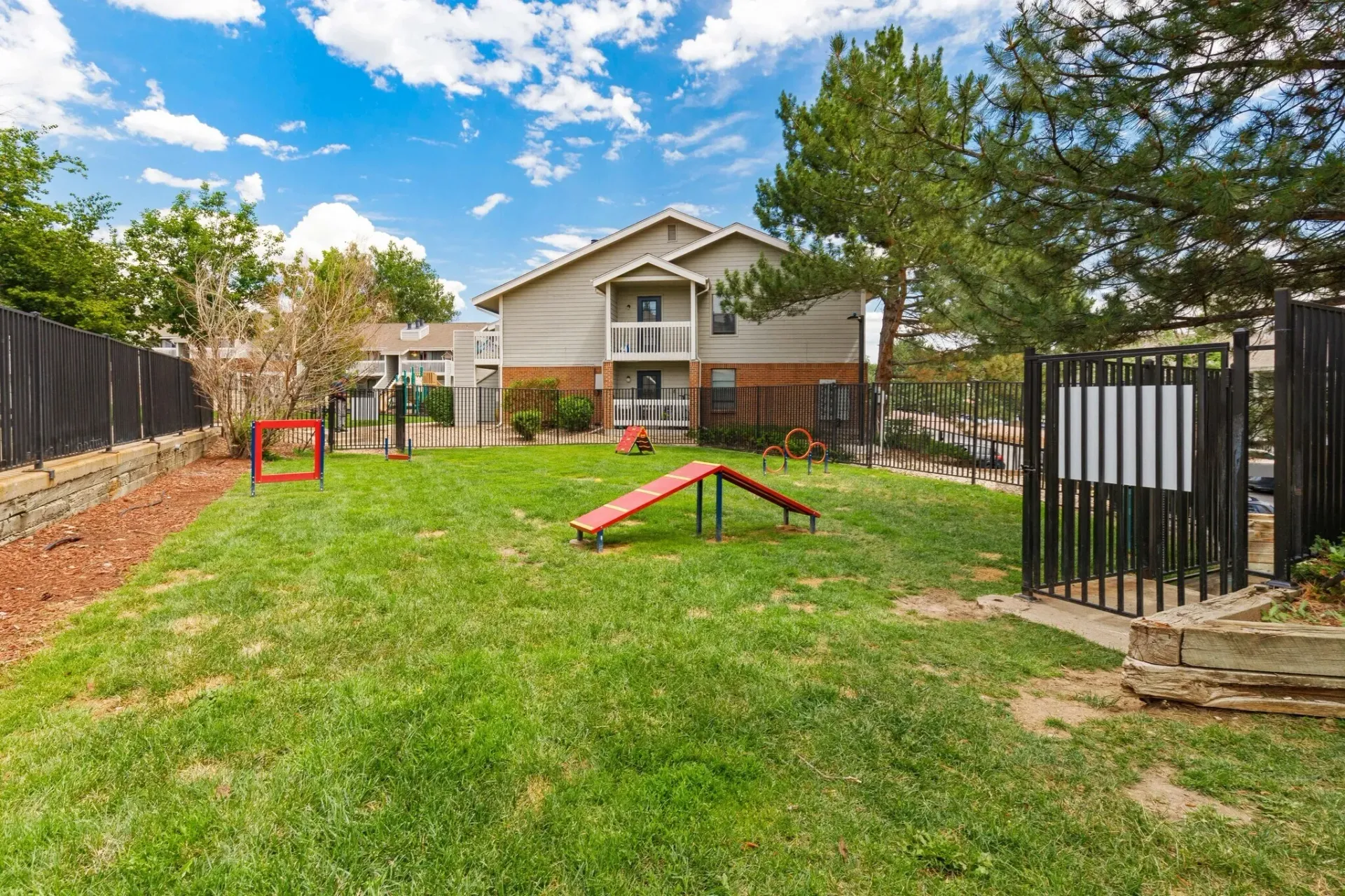 Dog park area with agility equipment, including ramps and tunnels, and a grassy lawn.