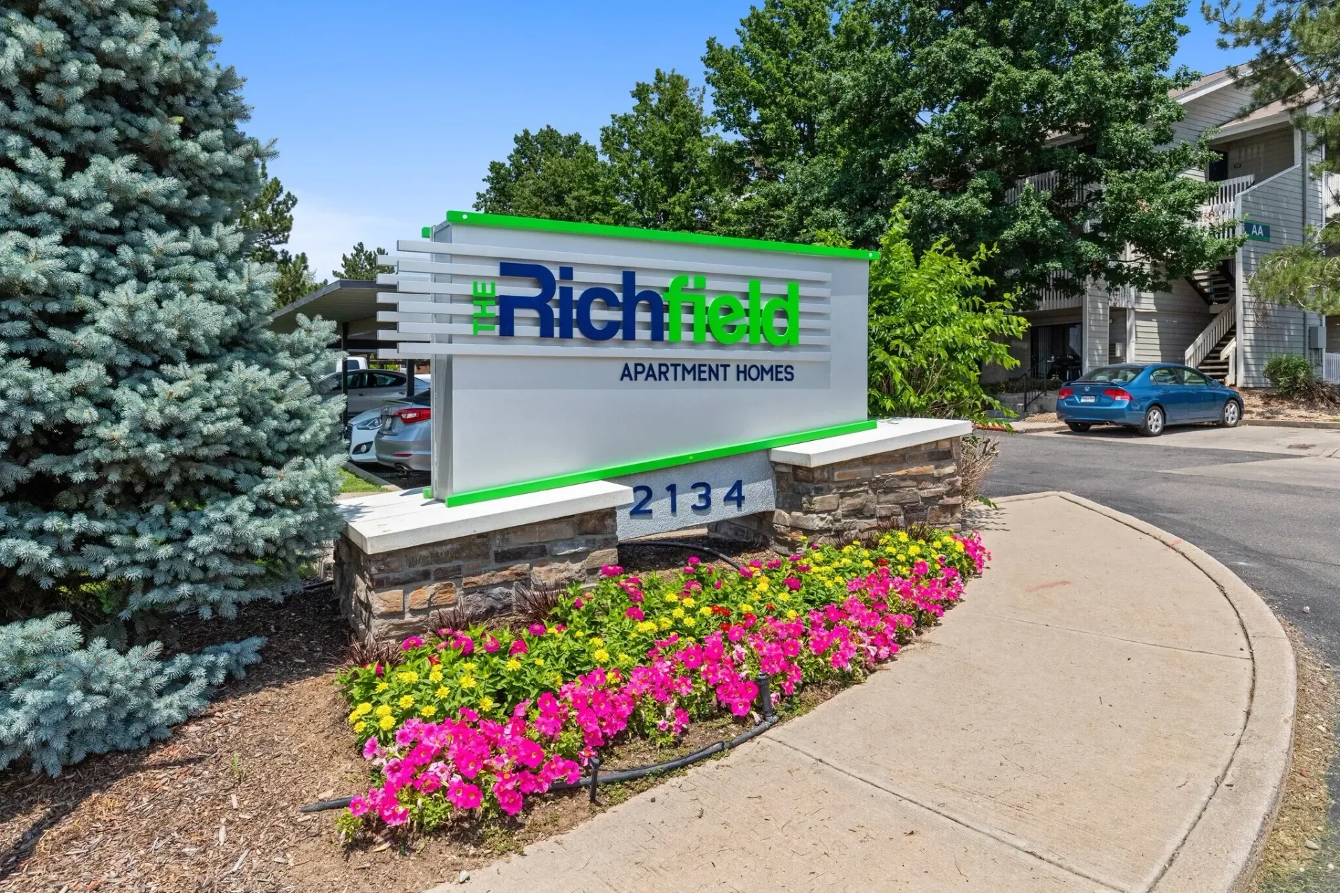The Richfield Apartment Homes monument sign with colorful flowers in front and a blue car parked nearby.