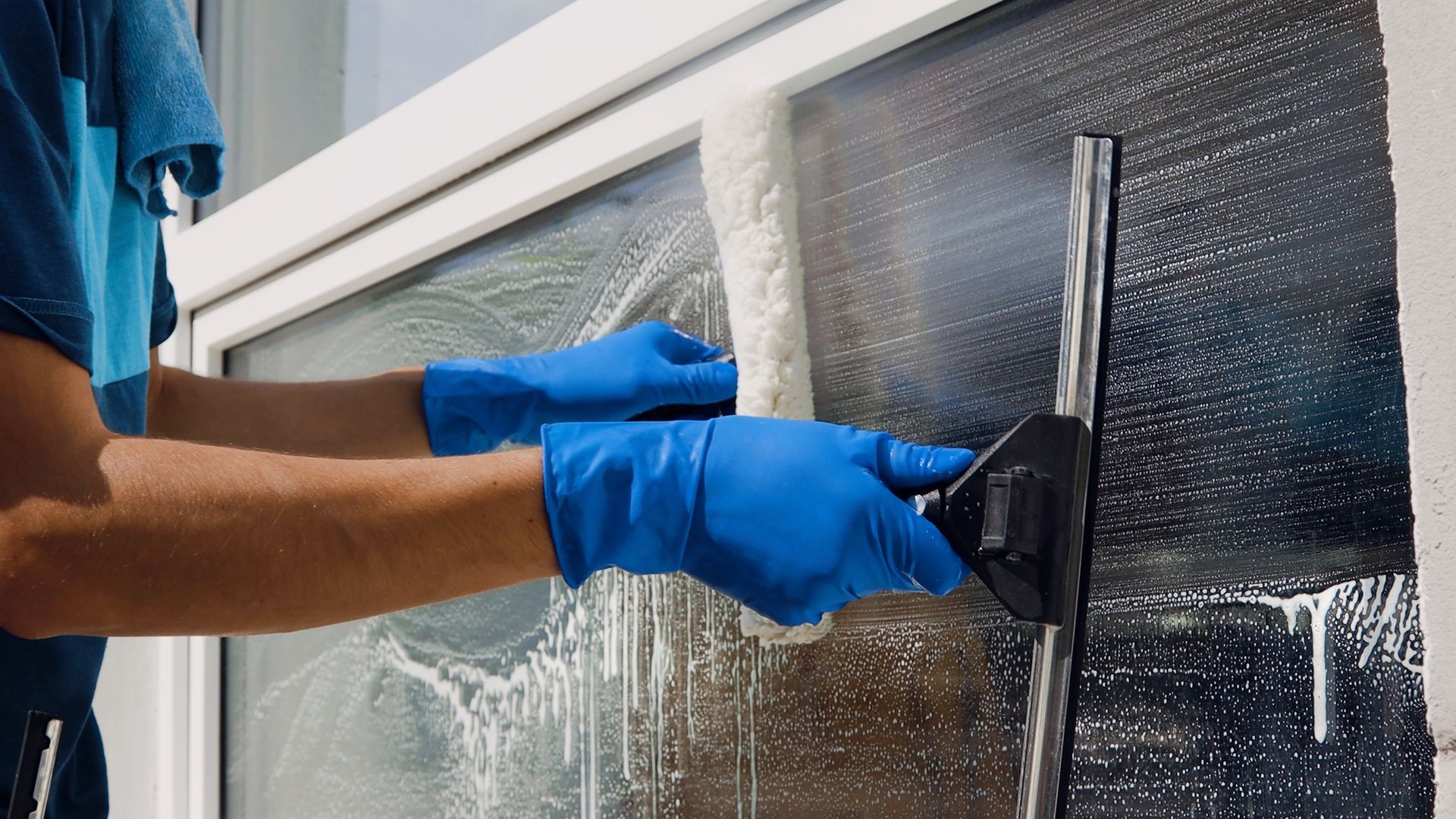 A person wearing blue gloves is cleaning a window with a squeegee.