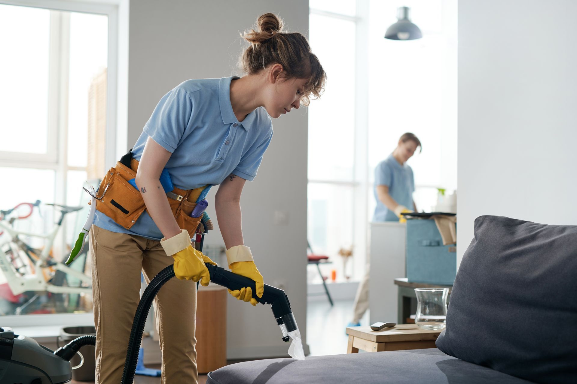 A woman is using a vacuum cleaner to clean a couch in a living room.