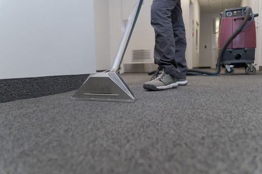 A person is cleaning a carpet with a vacuum cleaner.