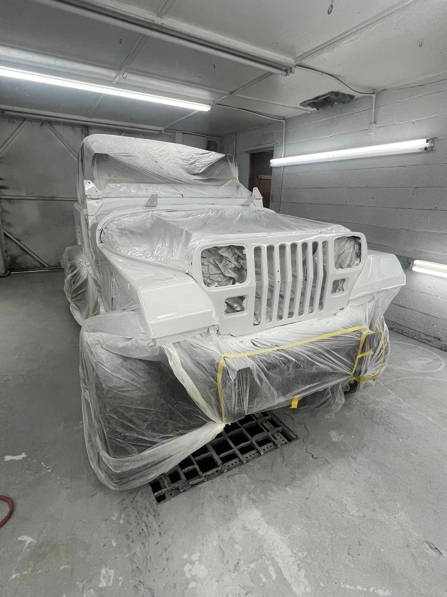 A jeep is covered in plastic wrap in a paint booth.
