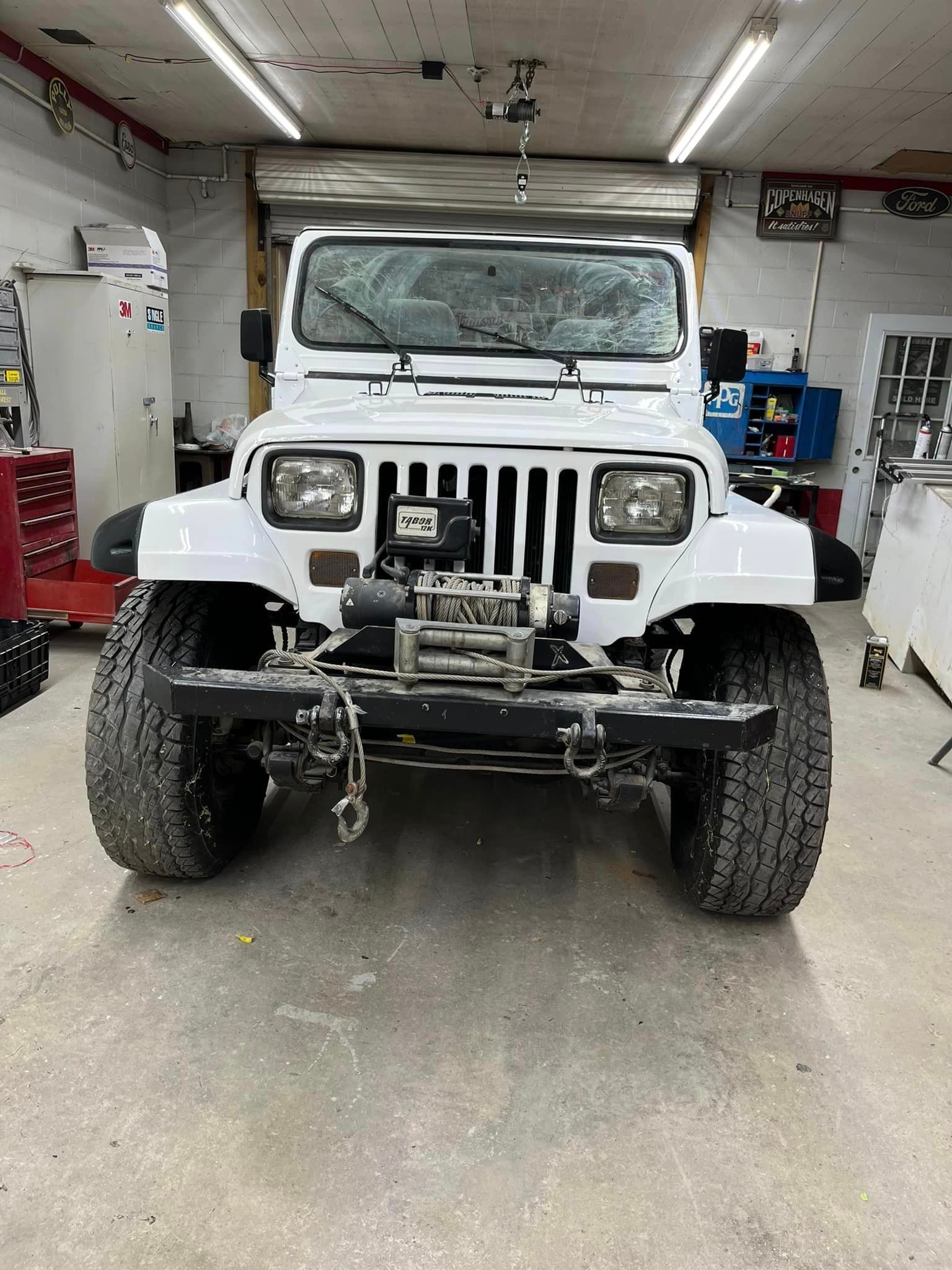 A white jeep is parked in a garage.