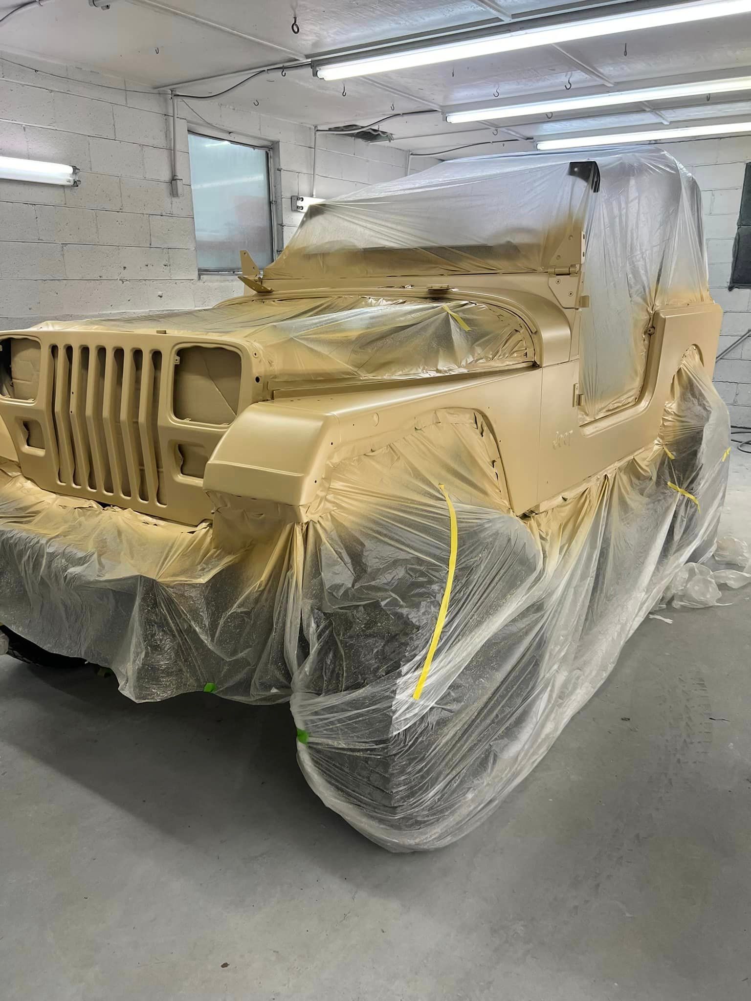A jeep is covered in plastic while being painted in a garage.