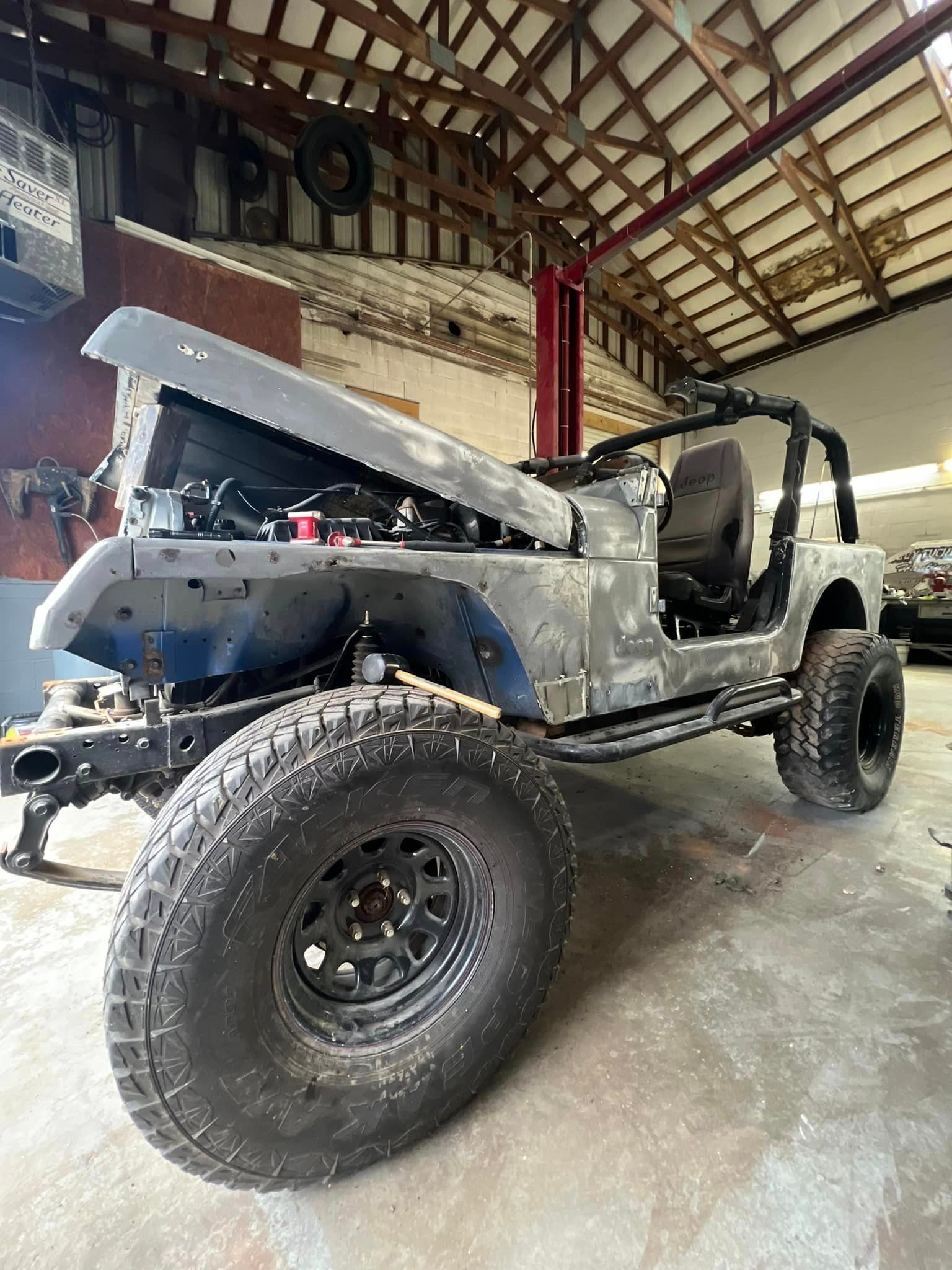 A jeep is sitting in a garage with the hood up.