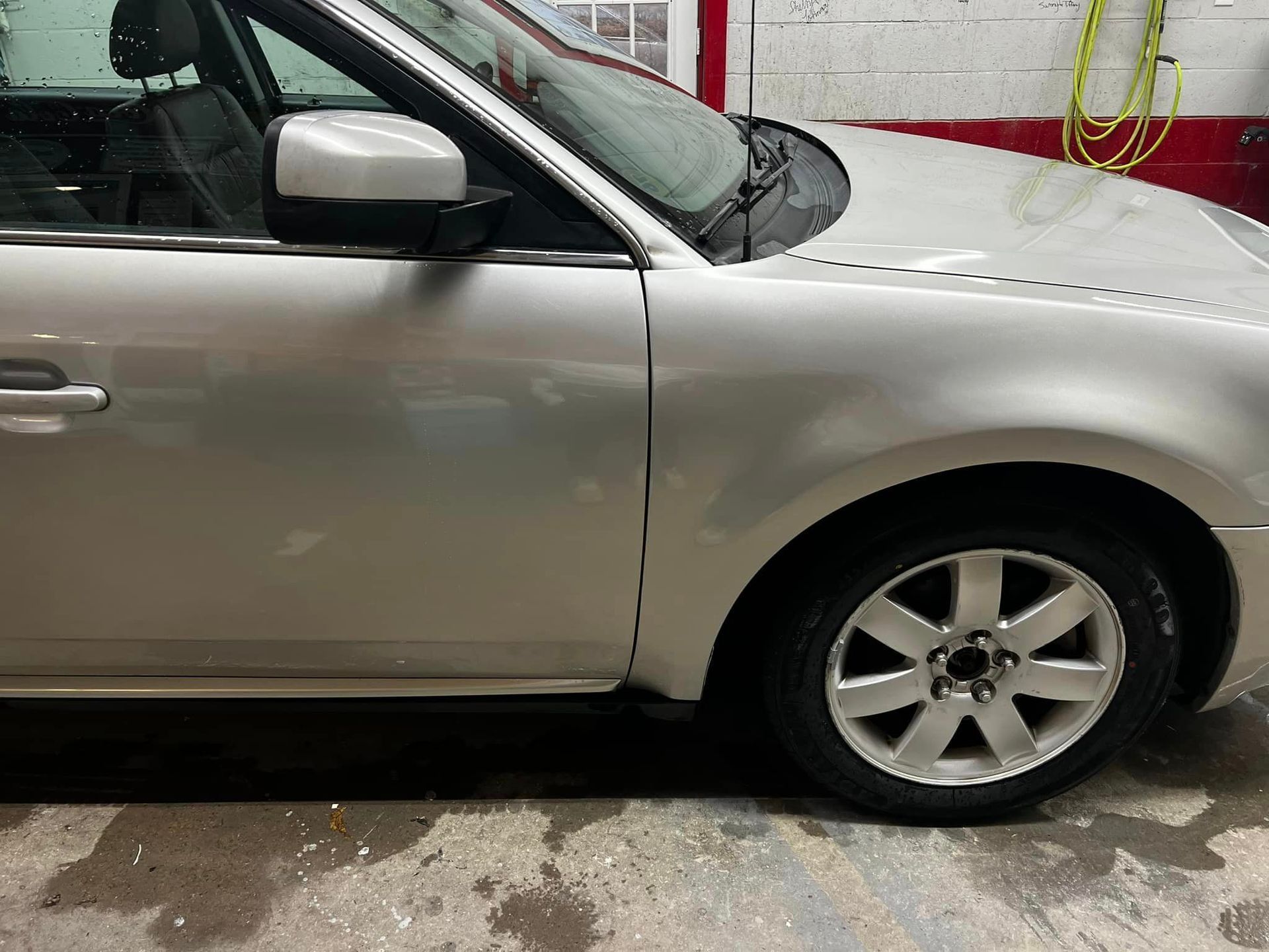 A silver car is parked in a garage next to a wall.