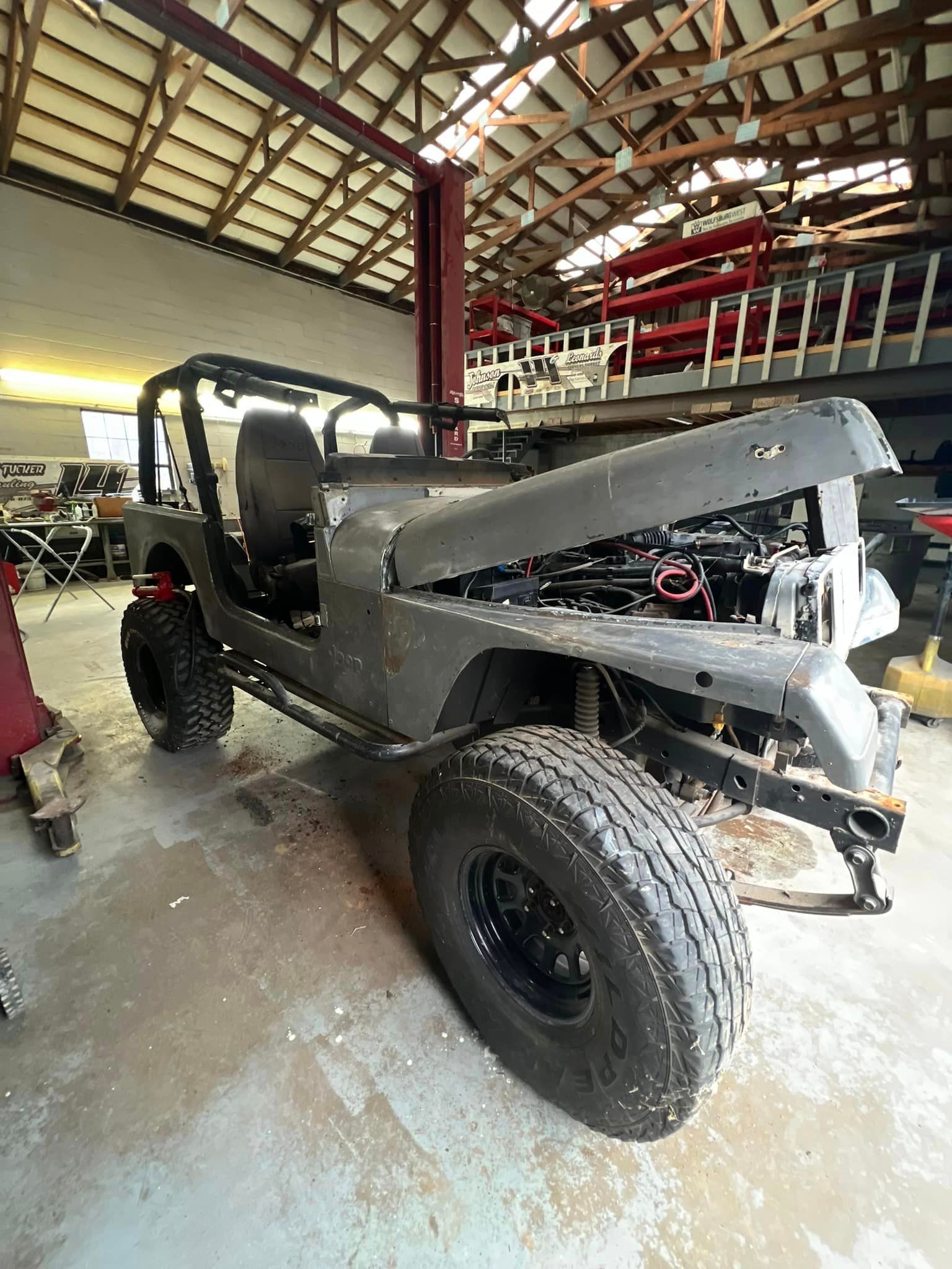 A jeep is sitting in a garage with the hood open.