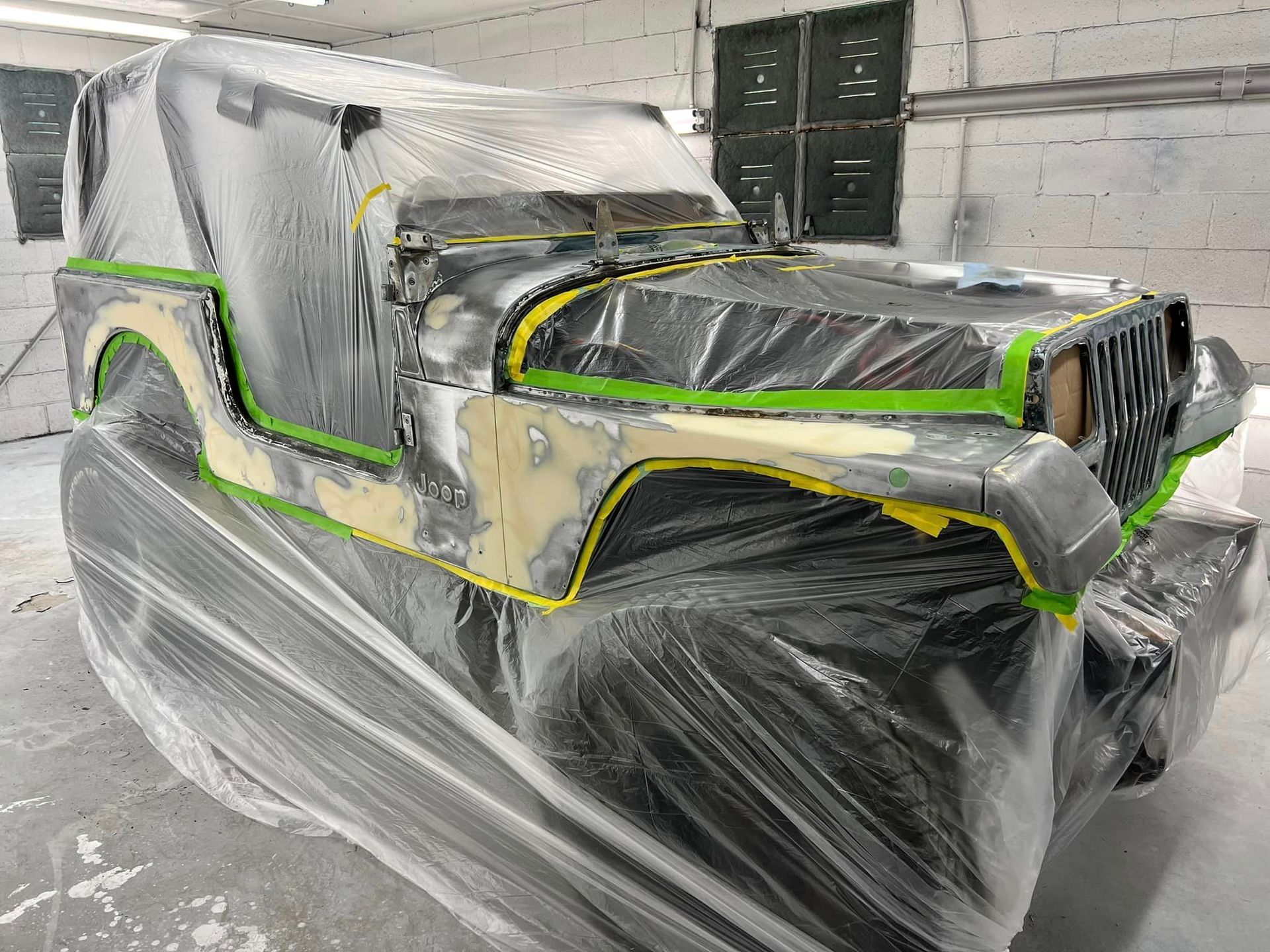 A jeep is wrapped in plastic while being painted in a garage.
