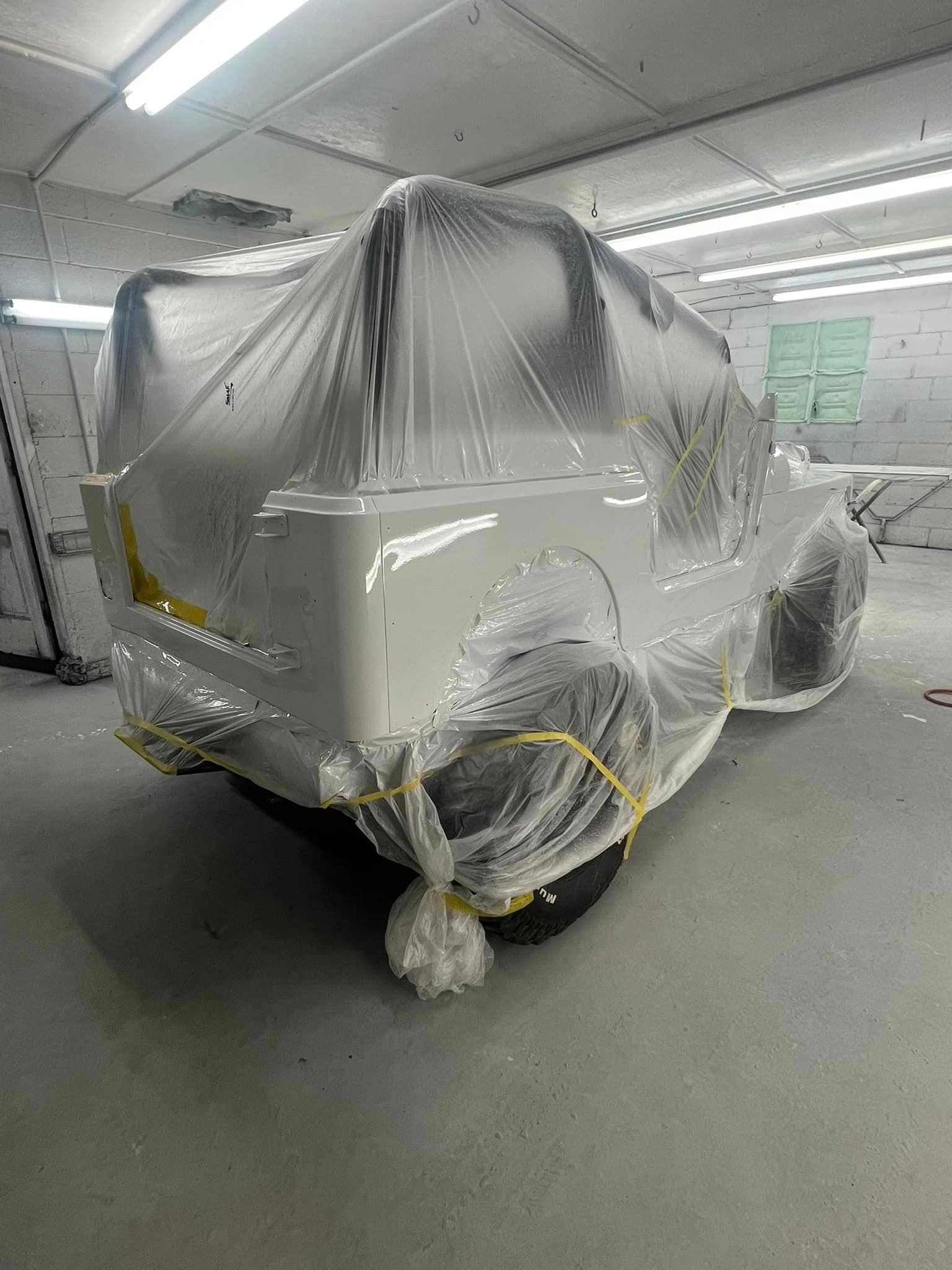 A white truck is covered in plastic in a paint booth.