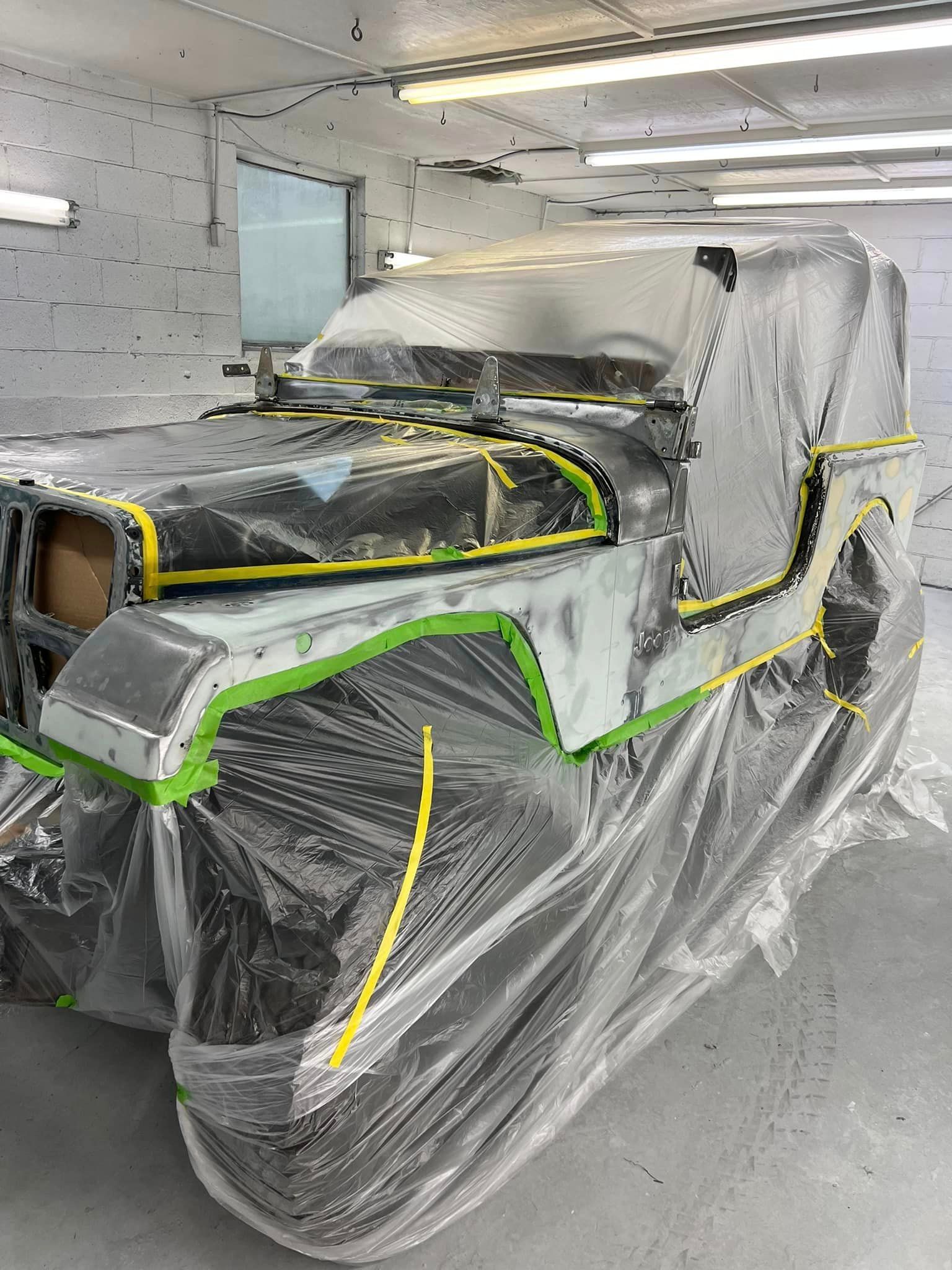 A jeep is covered in plastic while being painted in a garage.
