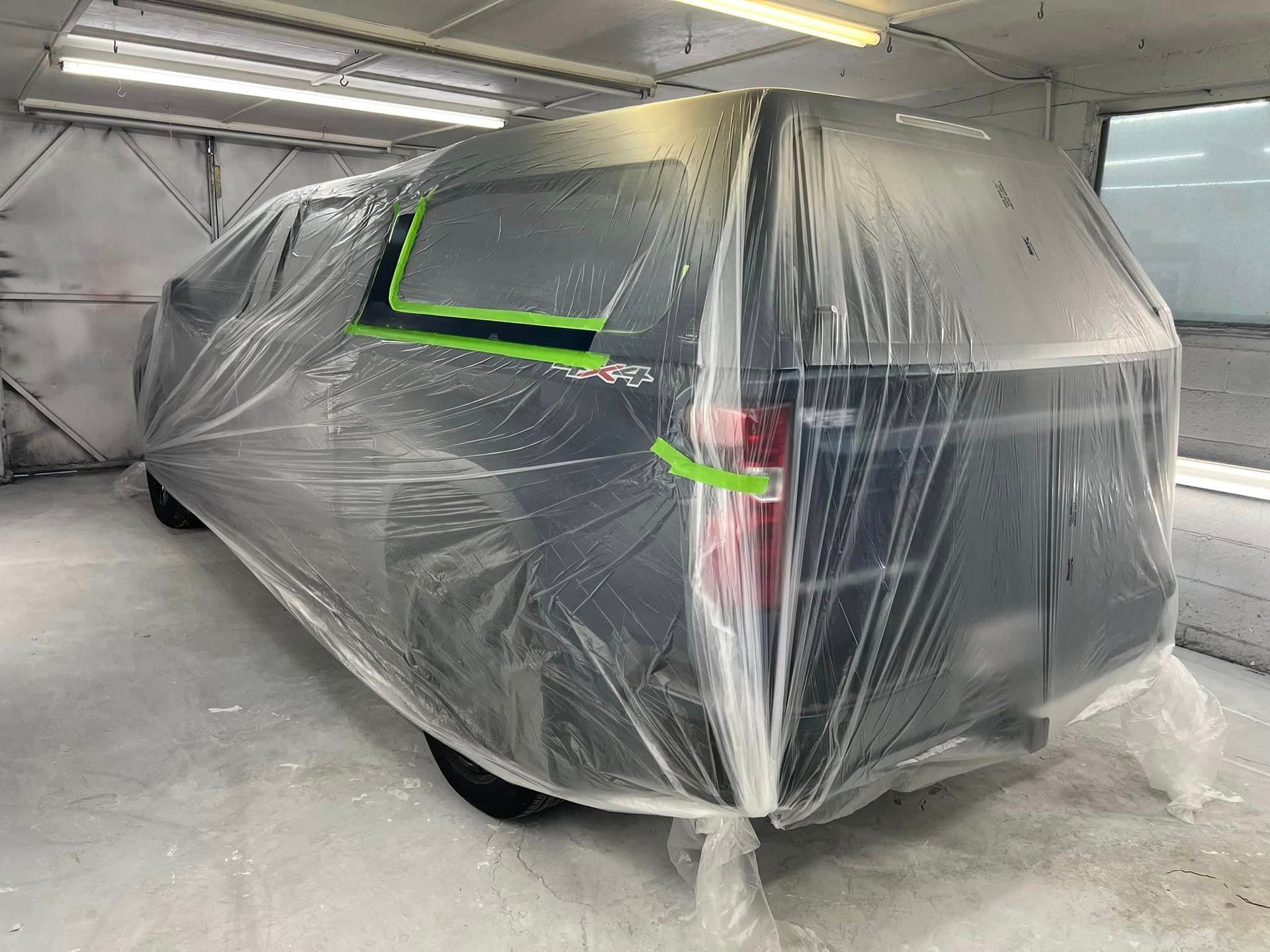 A car is covered in plastic in a paint booth.