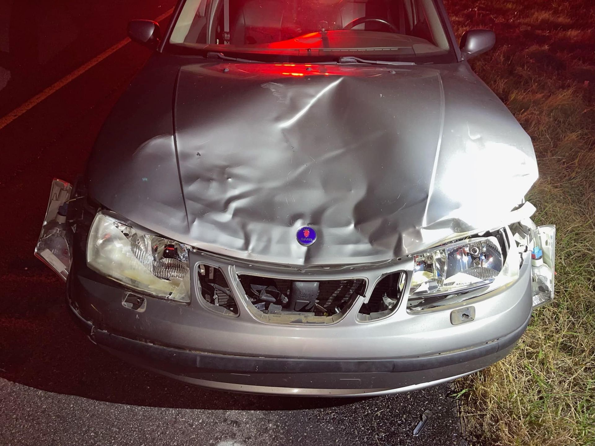 A silver car with a damaged hood is parked on the side of the road