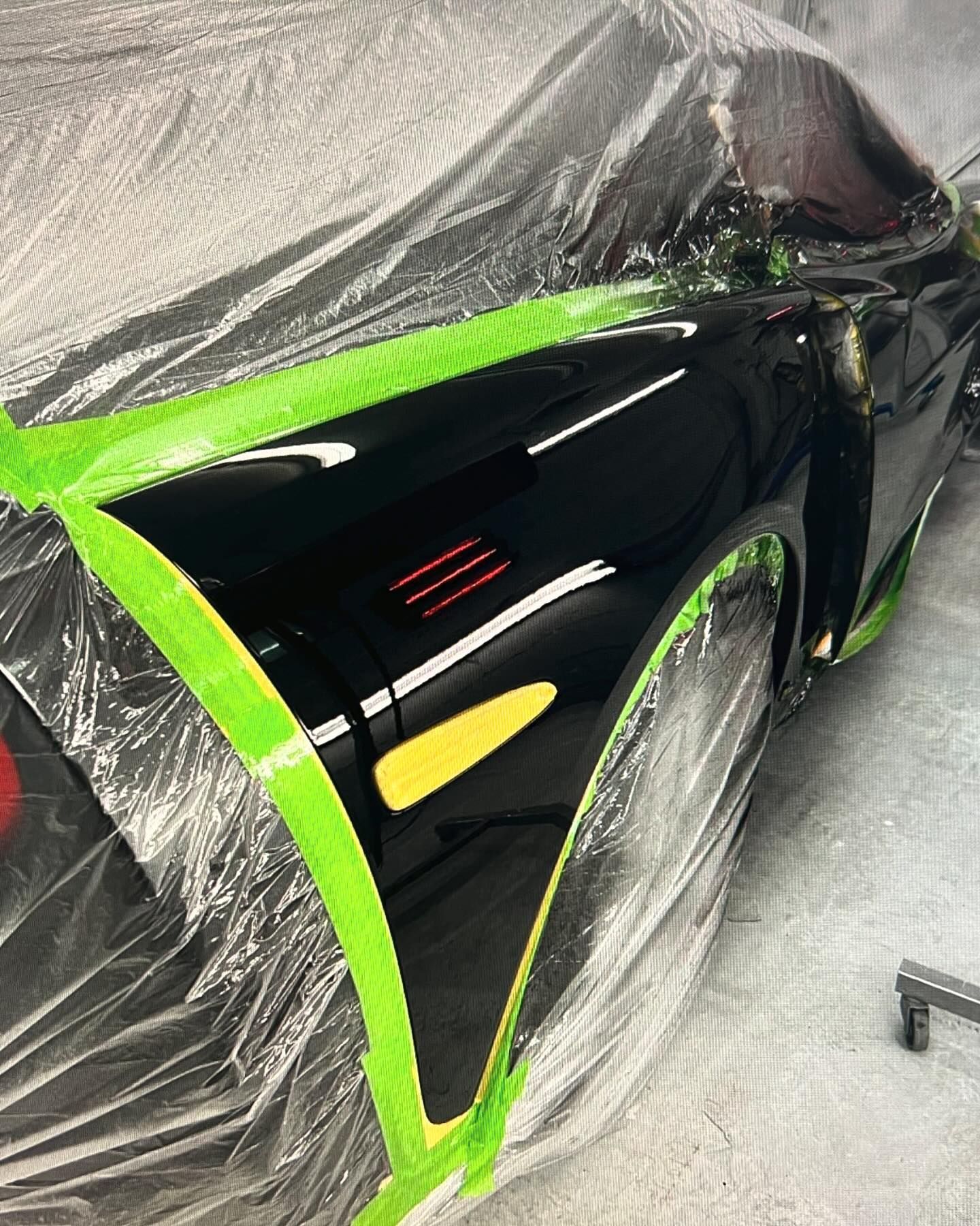 A black car is covered in plastic and green tape.