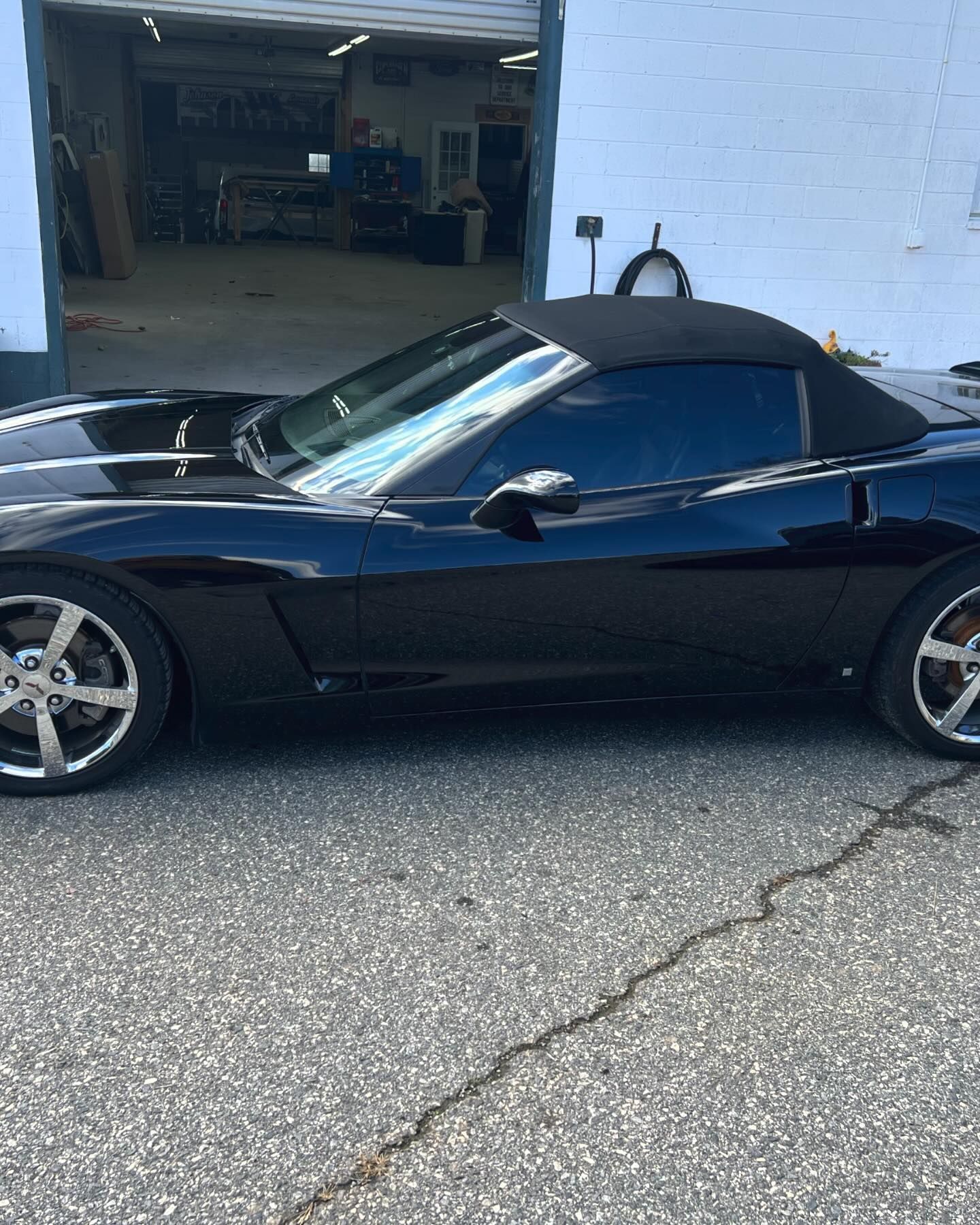 A black convertible corvette is parked in front of a garage.