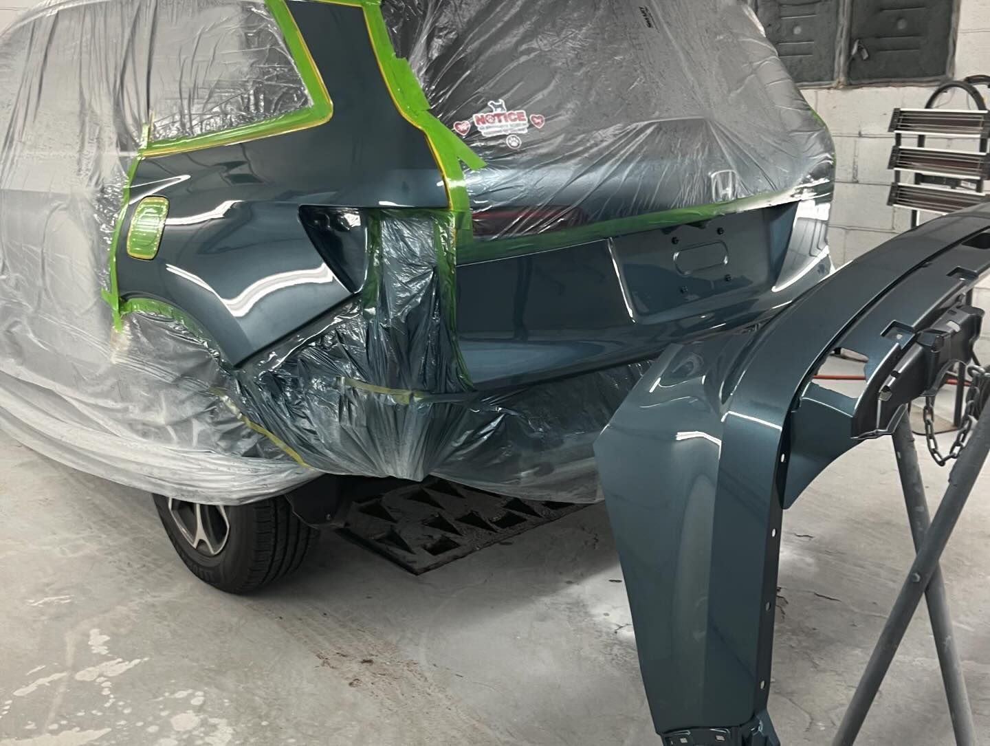 A car is covered in plastic and is being painted