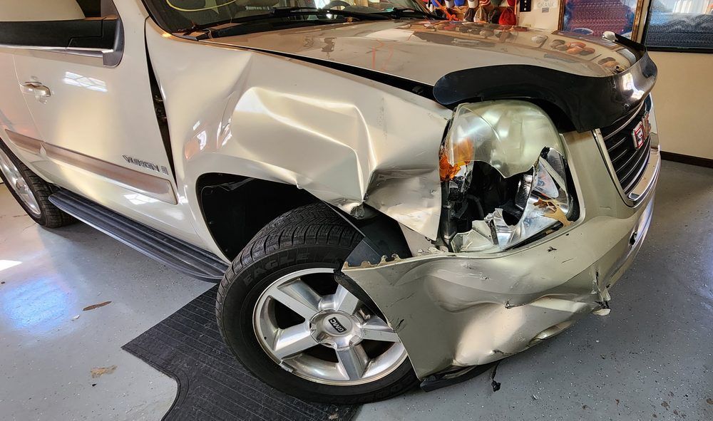 A silver suv with a damaged front end is parked in a garage.