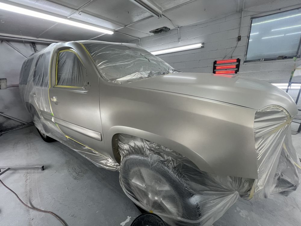 A silver suv is covered in plastic wrap in a paint booth.