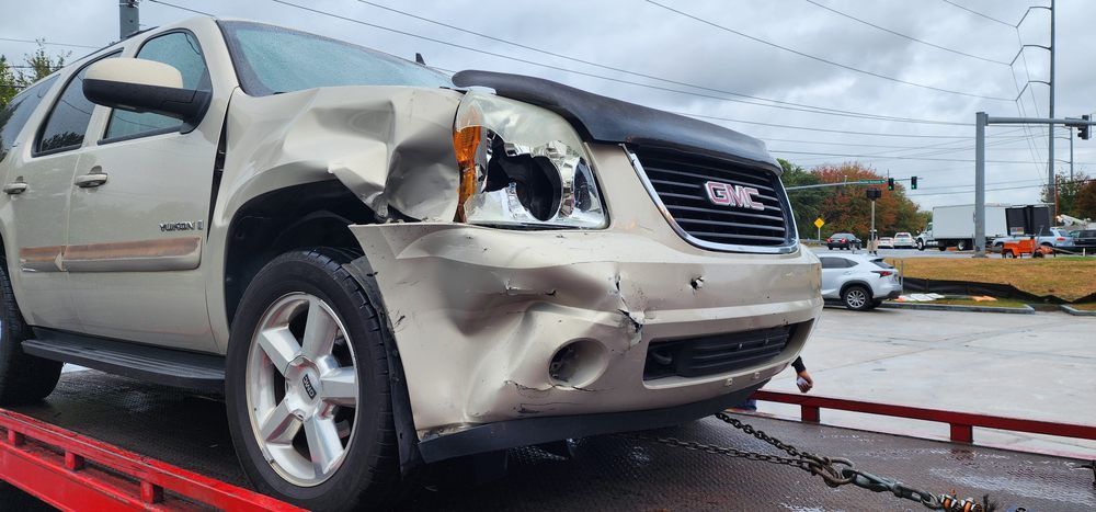 A damaged car is sitting on top of a red tow truck.