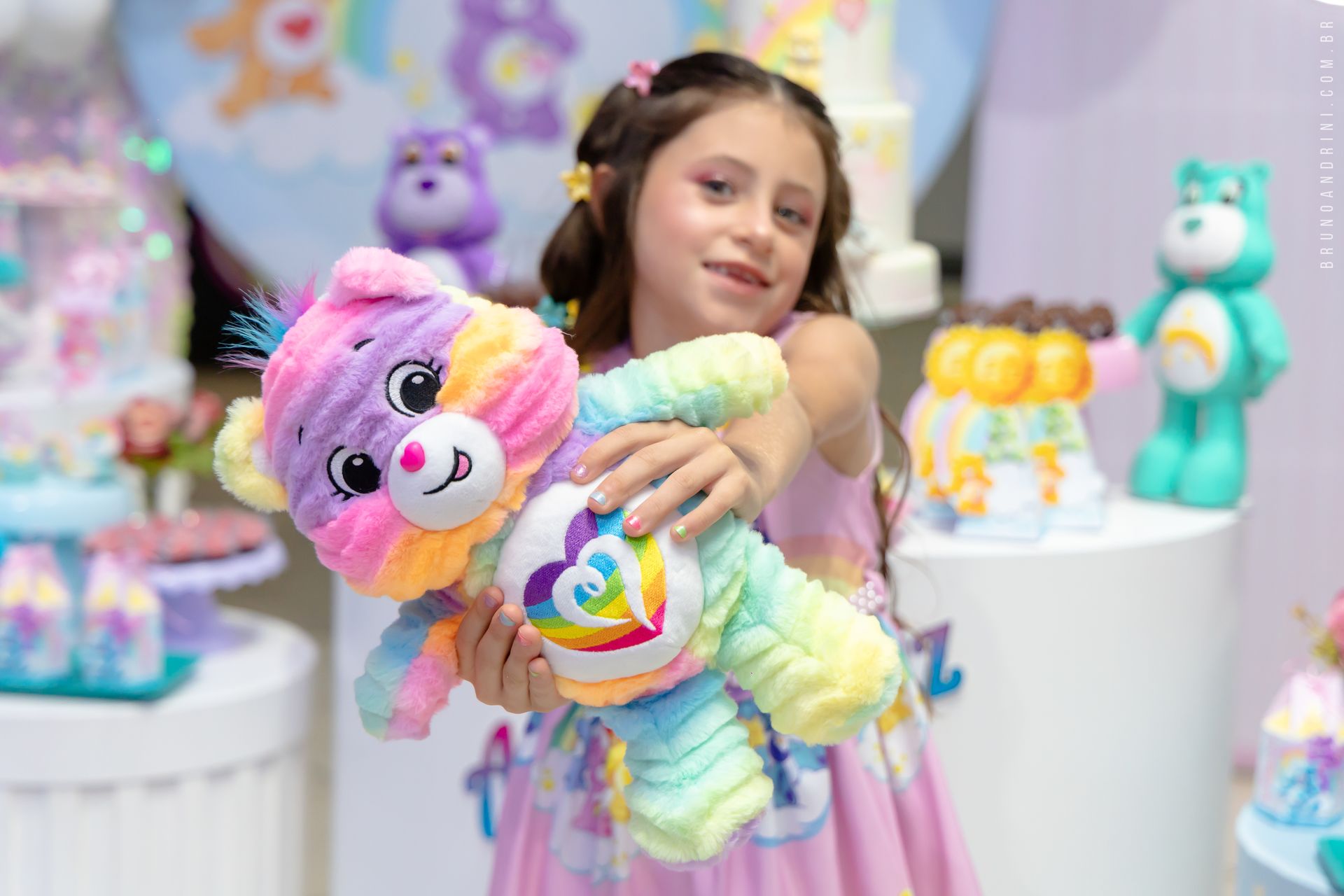 Girl holding a colorful Care Bear plush at a Care Bear-themed party.