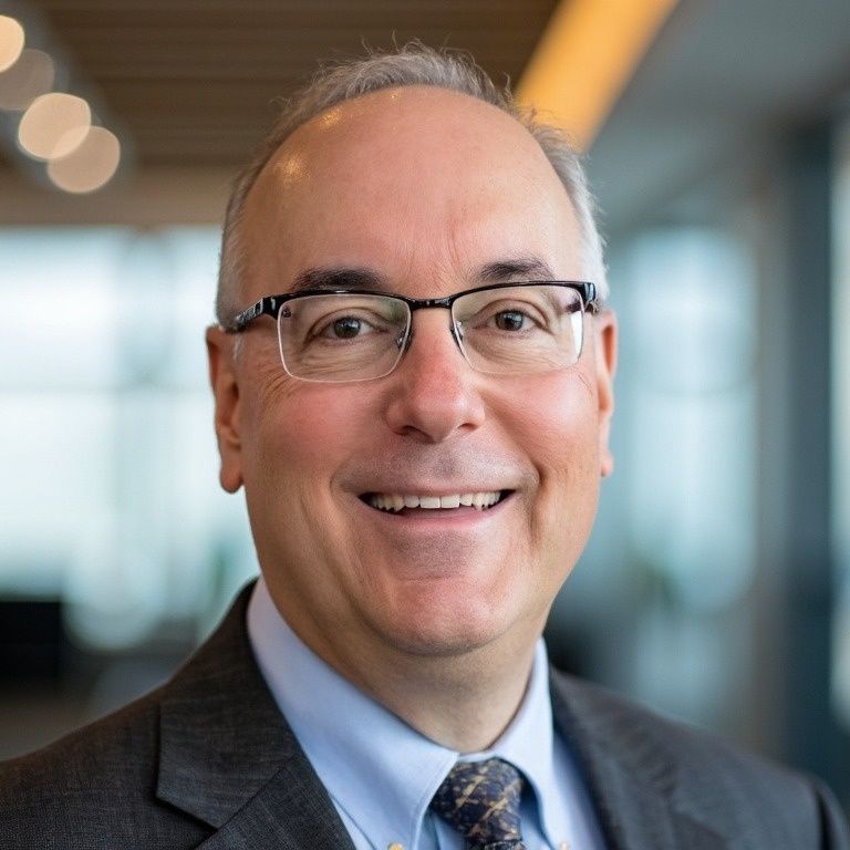 Man wearing glasses and a suit, smiling in a modern office setting.