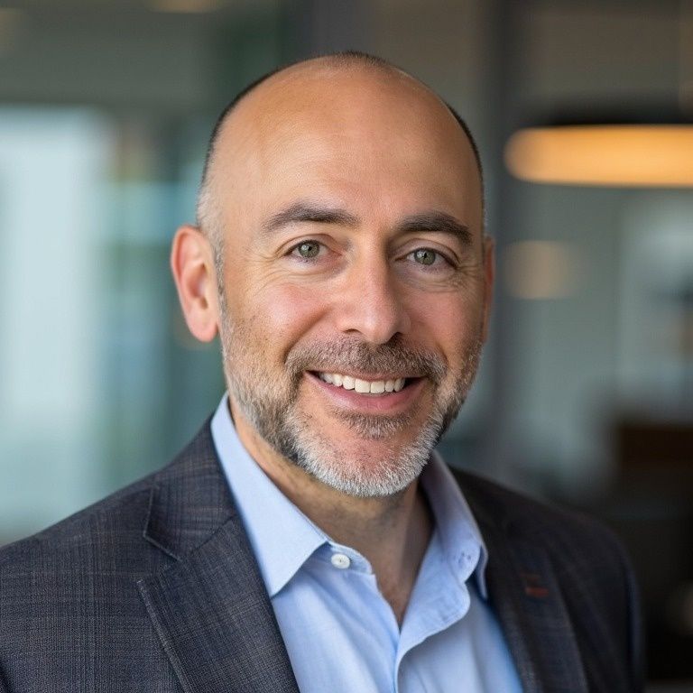 Smiling man with a receding hairline, wearing a blue shirt and grey blazer.