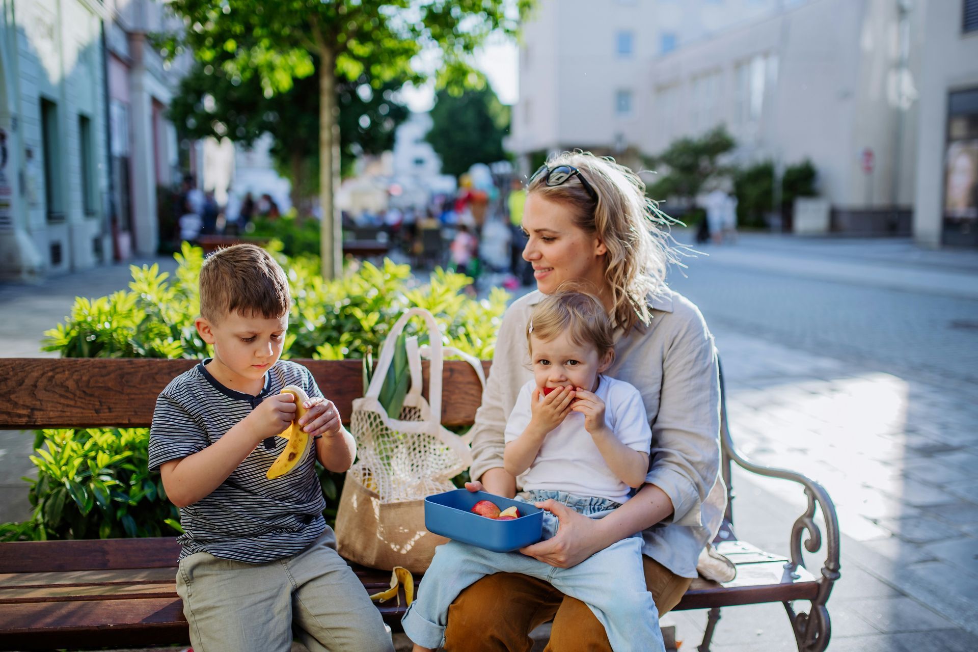 Woman with two children eating snacks on a park bench.