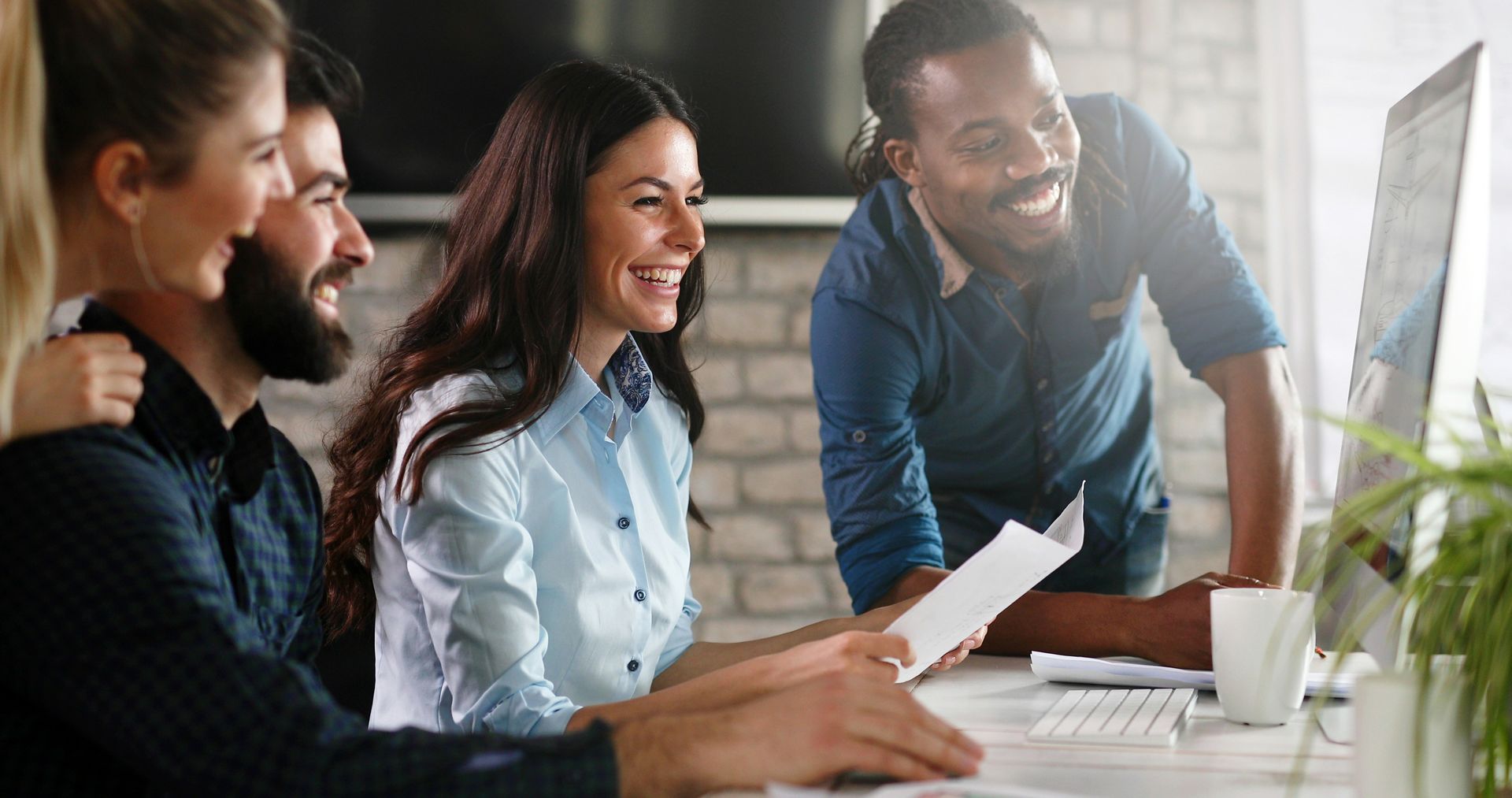 People smiling, looking at a computer screen in an office. They appear to be discussing a document.