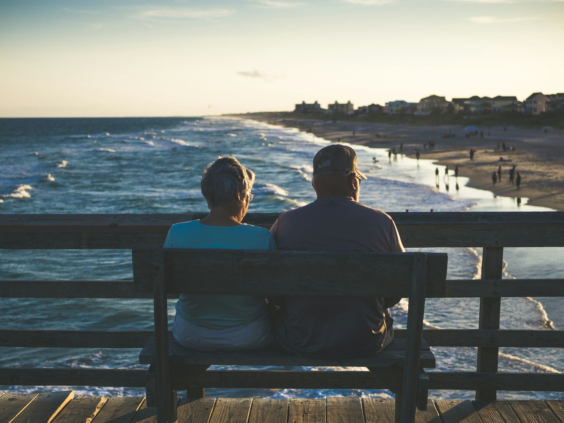 Couple on a wooden bench, overlooking the ocean at sunset.