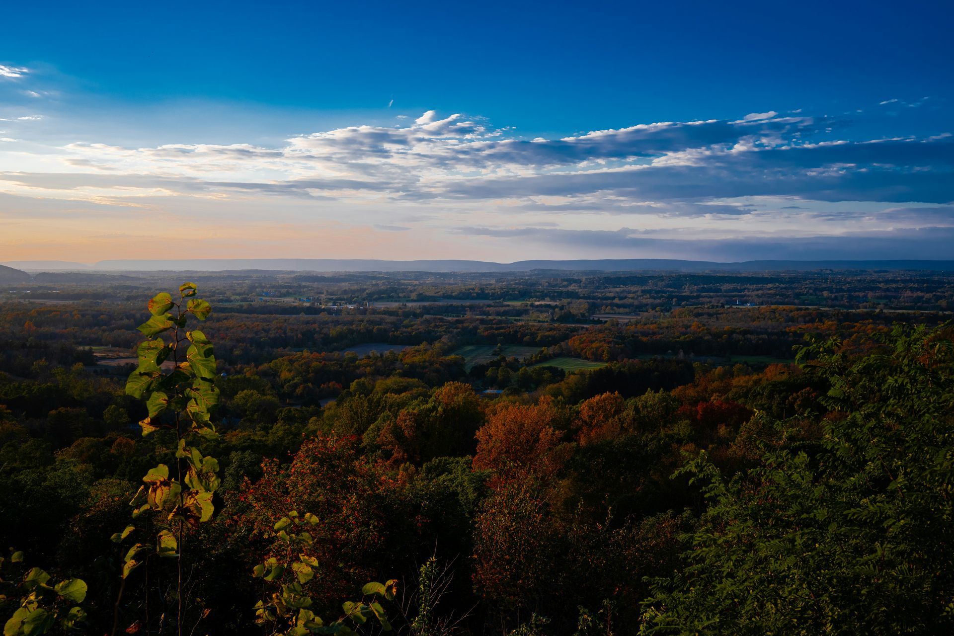 Overlooking a vast landscape of forests under a blue and cloudy sky during sunset.