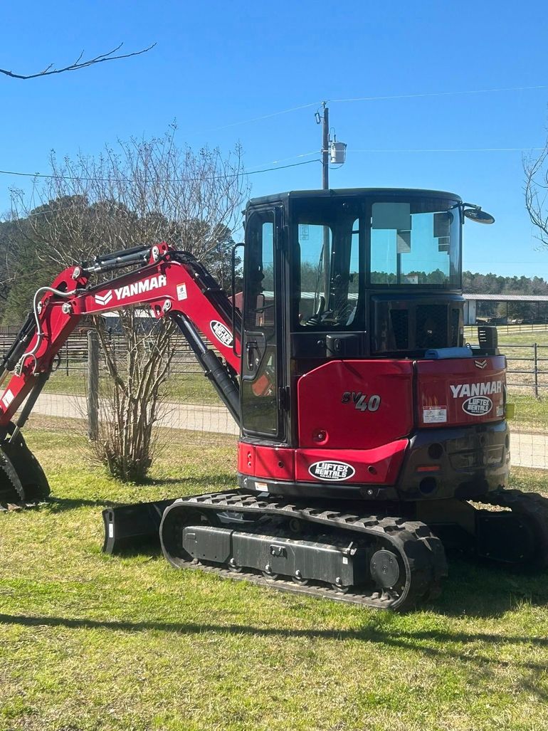 A bright red Yanmar VIO excavator parked on a grass field under a clear blue sky.
