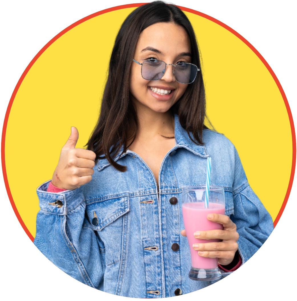 a woman in a denim jacket is holding a pink milkshake and giving a thumbs up .