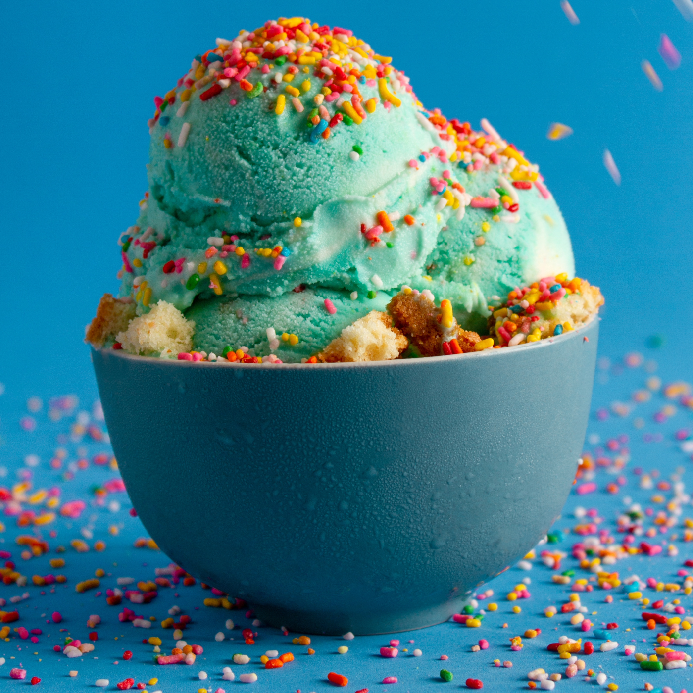 A teal bowl of a teal ice cream with sprinkles on it against a blue background