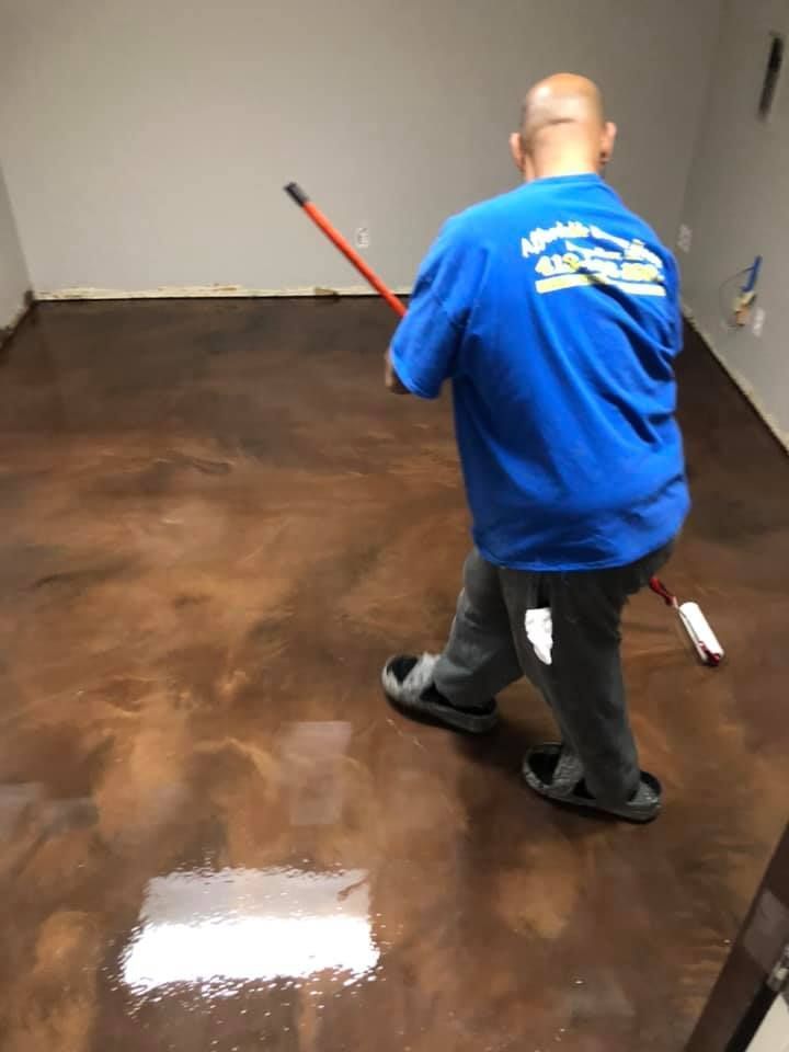 Person applying floor coating with a roller in a room with brown metallic floor.