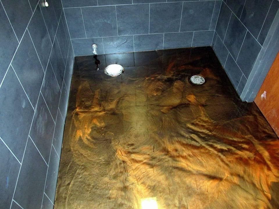 Dark metallic-colored epoxy floor with black tiled walls and two drain openings in a shower.