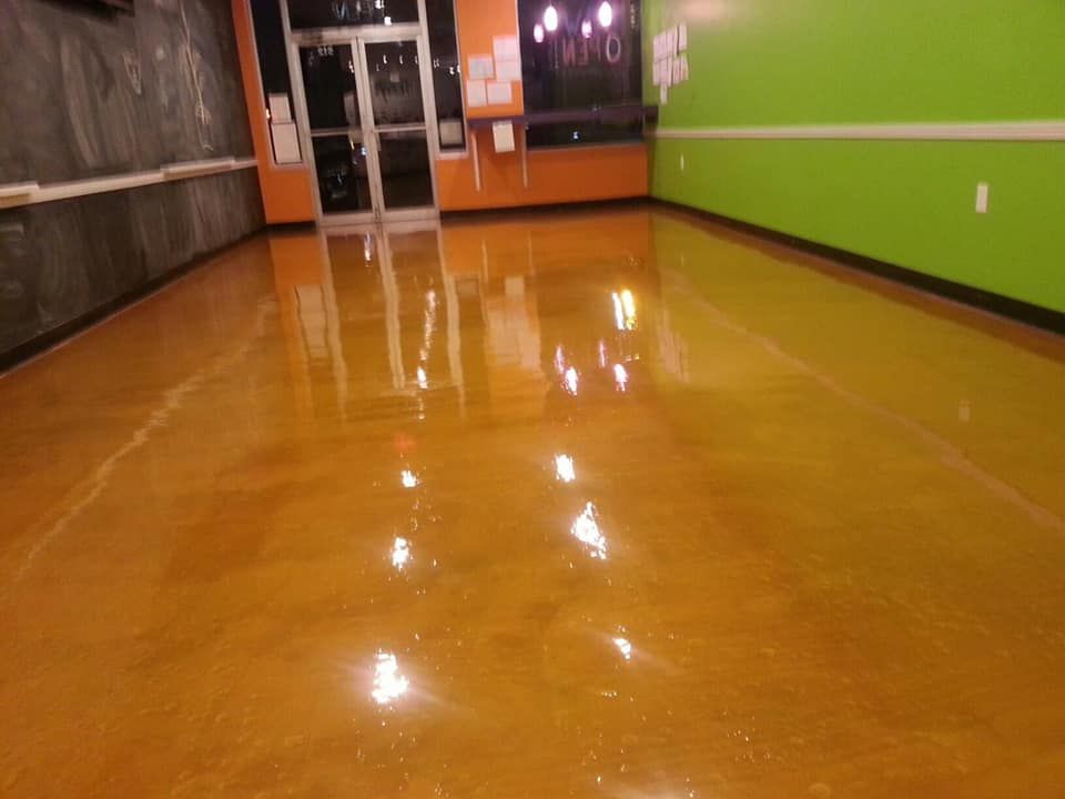 Shiny, amber-colored epoxy floor in a brightly painted, empty commercial space. Entrance door visible.