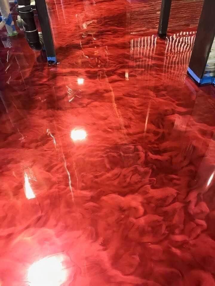 Red, glossy epoxy floor with swirling patterns and reflections of a room's elements.