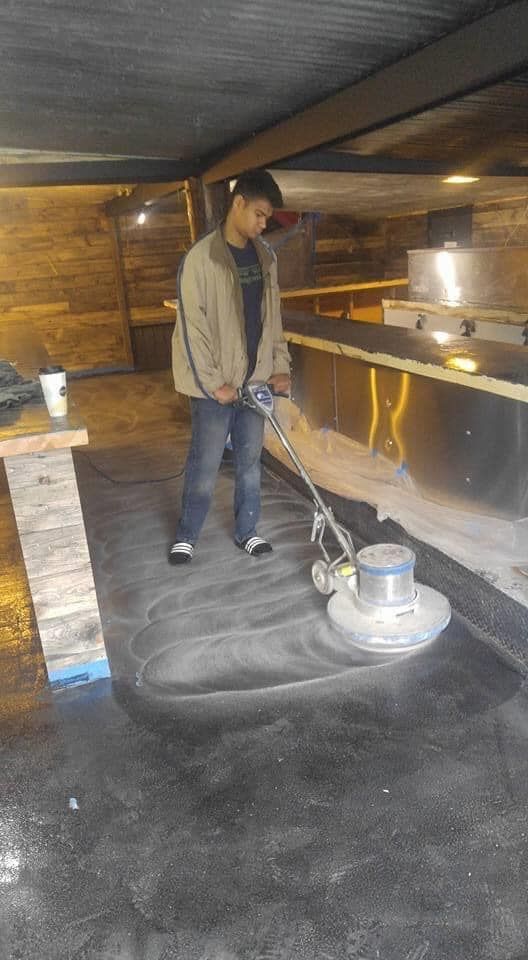 Person using a floor buffer on a dark, possibly concrete, surface indoors.