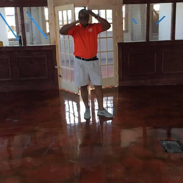 Man in orange shirt and white shorts standing on a shiny, reddish floor, arms raised.